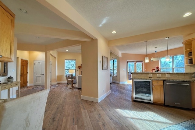 kitchen featuring stainless steel dishwasher, light wood-type flooring, a textured ceiling, decorative light fixtures, and beverage cooler