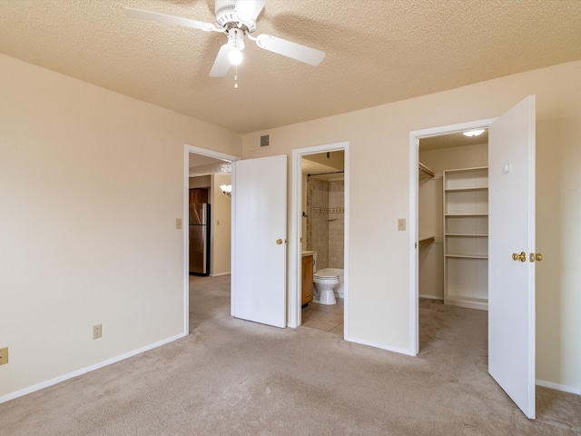 unfurnished bedroom featuring a walk in closet, ensuite bath, ceiling fan, stainless steel fridge, and light colored carpet