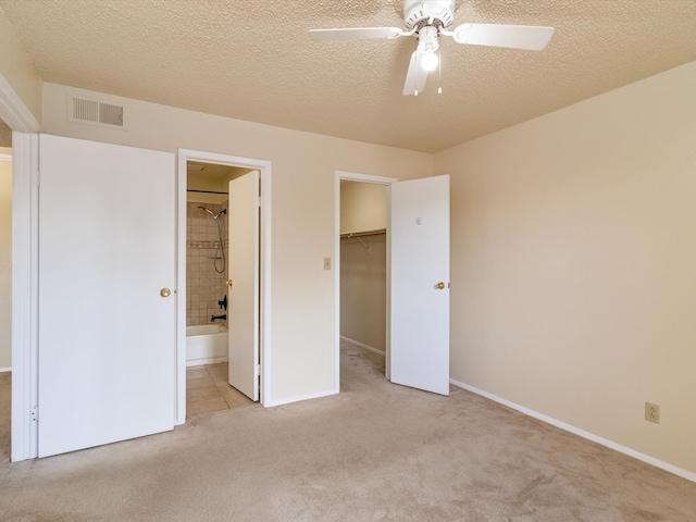 unfurnished bedroom featuring a textured ceiling, connected bathroom, light colored carpet, and ceiling fan