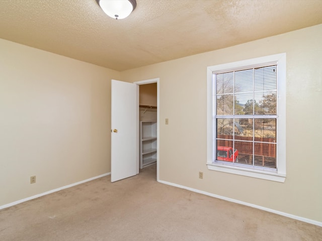 unfurnished bedroom with light carpet, a textured ceiling, a spacious closet, and a closet