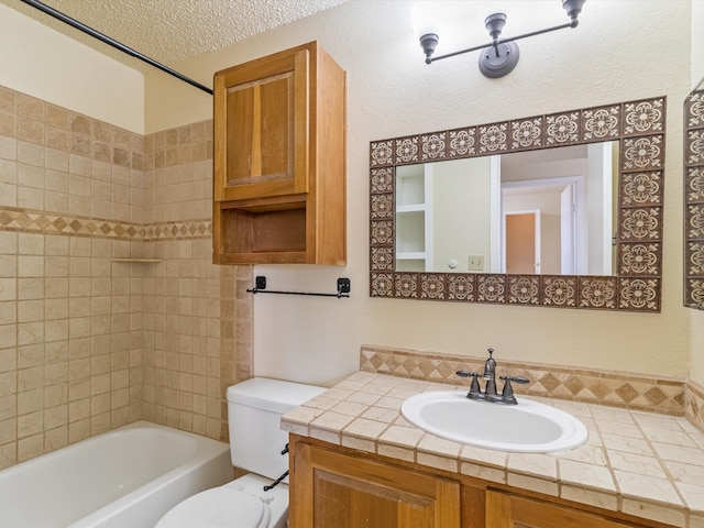 full bathroom with tiled shower / bath, vanity, a textured ceiling, and toilet