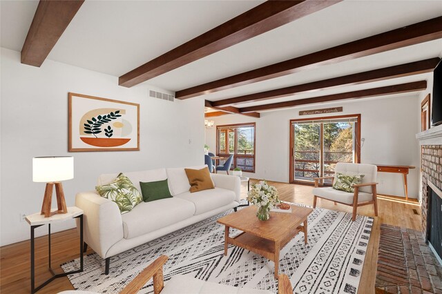 living room with beam ceiling, light hardwood / wood-style flooring, built in features, and a brick fireplace