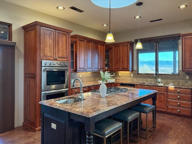 kitchen featuring a center island with sink, sink, appliances with stainless steel finishes, dark hardwood / wood-style flooring, and light stone counters