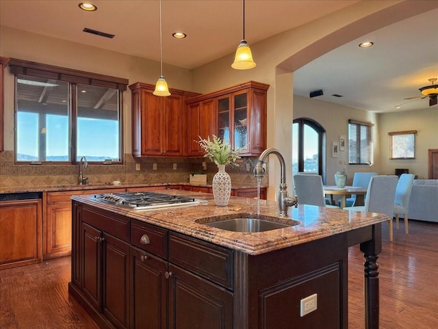 kitchen featuring tasteful backsplash, a kitchen island with sink, dark hardwood / wood-style floors, and stainless steel gas cooktop