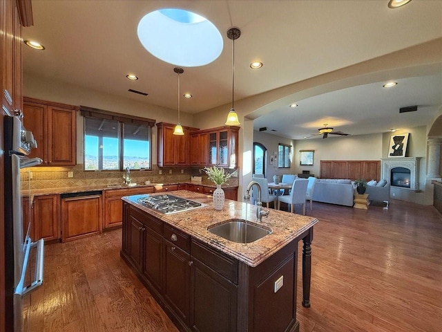 kitchen with ceiling fan, sink, stainless steel gas cooktop, dark hardwood / wood-style floors, and a center island with sink