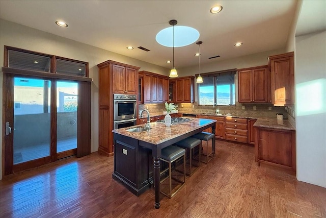 kitchen with light stone countertops, tasteful backsplash, dark wood-type flooring, a center island with sink, and a breakfast bar area