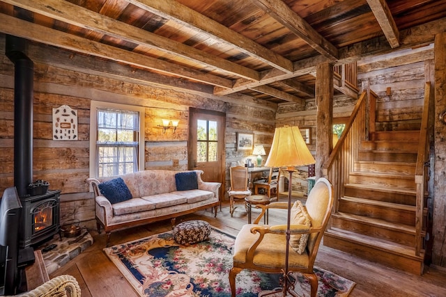 living area with beam ceiling, wood-type flooring, a wood stove, and wooden ceiling