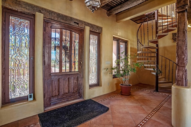 foyer with beam ceiling, a wealth of natural light, and light tile patterned flooring