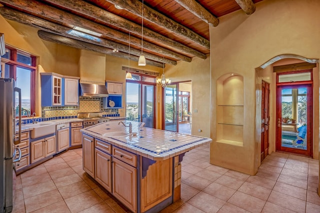 kitchen with tile counters, beamed ceiling, an island with sink, light tile patterned floors, and wood ceiling