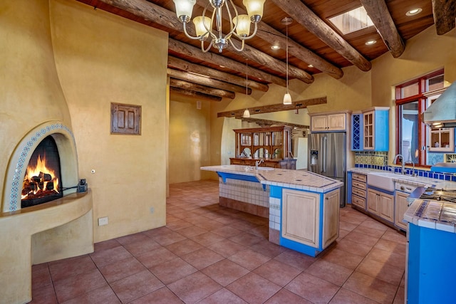 kitchen featuring sink, beam ceiling, tile countertops, an island with sink, and light tile patterned flooring