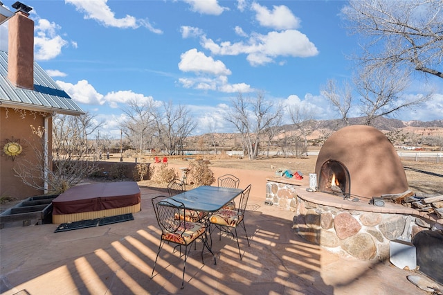 view of patio featuring grilling area, exterior fireplace, a mountain view, and a hot tub