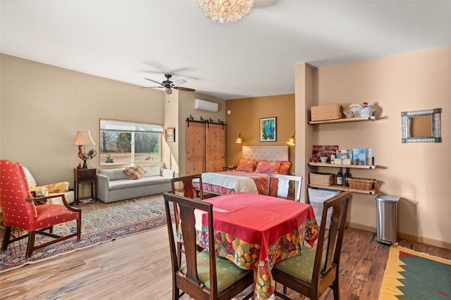 dining area with ceiling fan, a barn door, an AC wall unit, and wood-type flooring