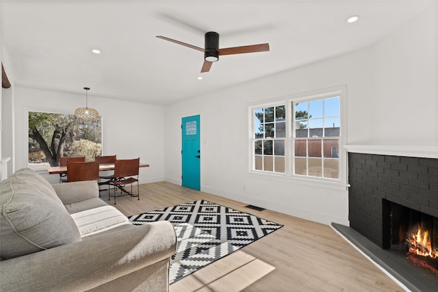 living room with ceiling fan, light wood-type flooring, and a brick fireplace