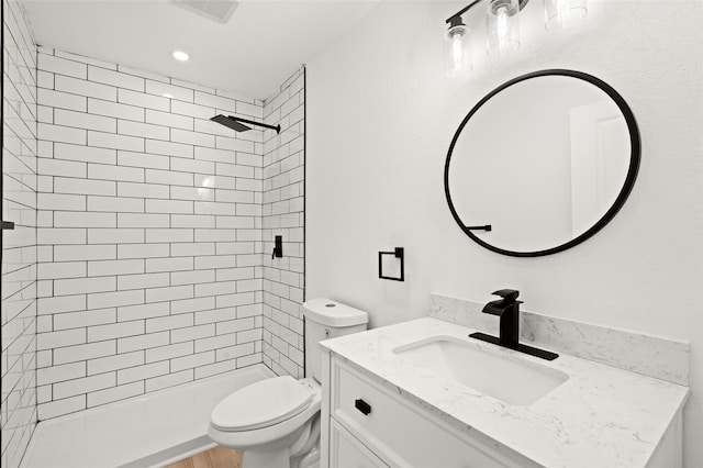 bathroom with a tile shower, vanity, and toilet