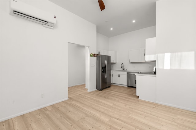 kitchen featuring sink, light wood-type flooring, a wall mounted AC, white cabinetry, and stainless steel appliances