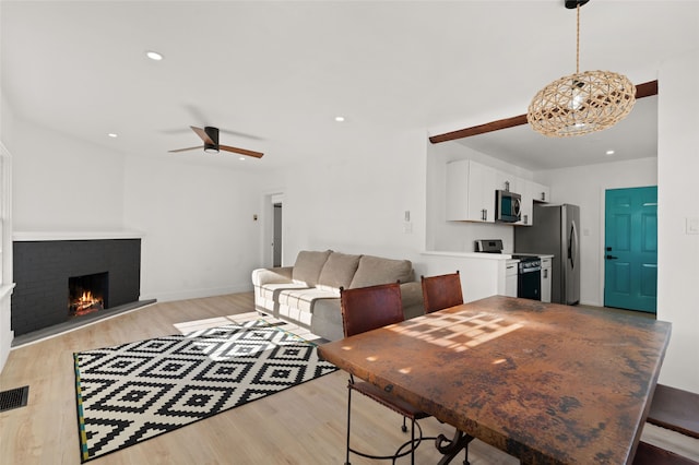 dining area with a fireplace, ceiling fan, and light hardwood / wood-style flooring