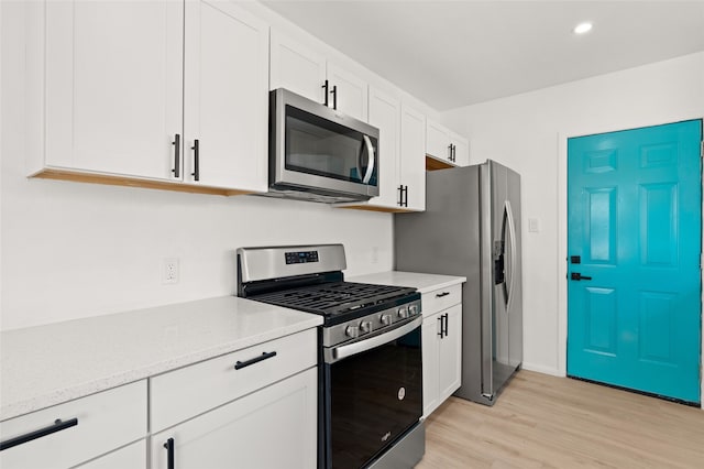 kitchen with white cabinets, light stone counters, appliances with stainless steel finishes, and light hardwood / wood-style flooring