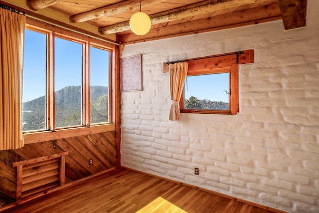 spare room with brick wall, beamed ceiling, wooden ceiling, a mountain view, and hardwood / wood-style floors