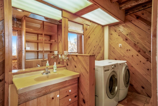 clothes washing area featuring separate washer and dryer, wooden walls, and sink