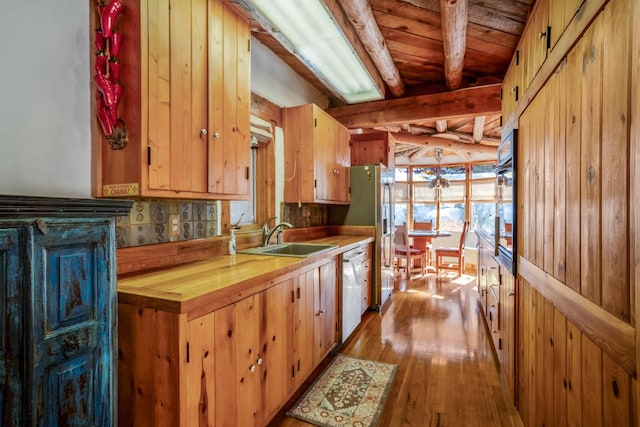 kitchen featuring beam ceiling, sink, wood counters, white dishwasher, and light hardwood / wood-style floors