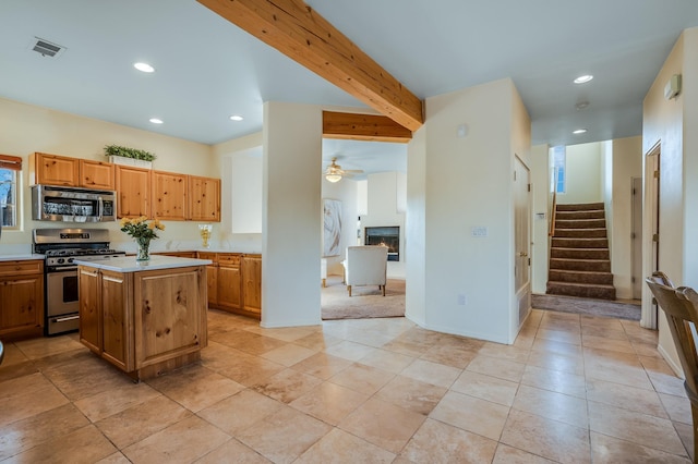 kitchen with appliances with stainless steel finishes, ceiling fan, beam ceiling, a fireplace, and a center island