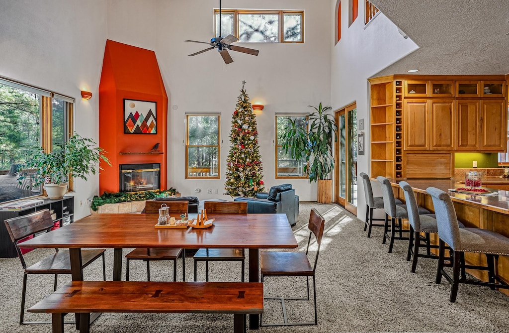 132 Aspen, Los Alamos, NM 87544 - dining space with a towering ceiling, a ceiling fan, light colored carpet, and a glass covered fireplace
