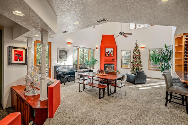 carpeted dining room with a wealth of natural light, a large fireplace, ceiling fan, and a textured ceiling