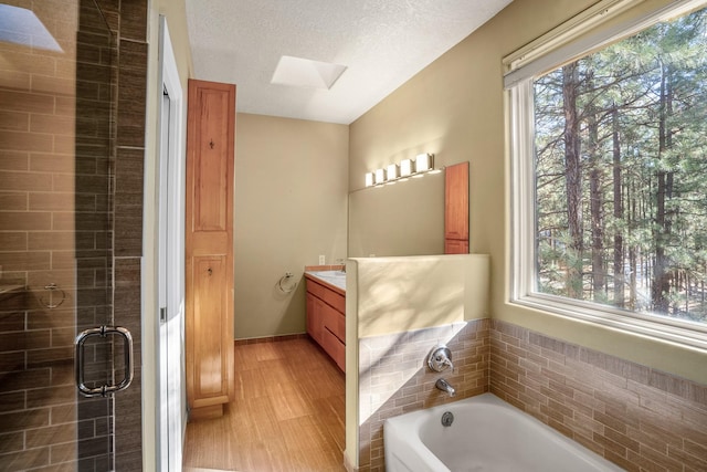 bathroom with separate shower and tub, hardwood / wood-style floors, a textured ceiling, vaulted ceiling with skylight, and vanity