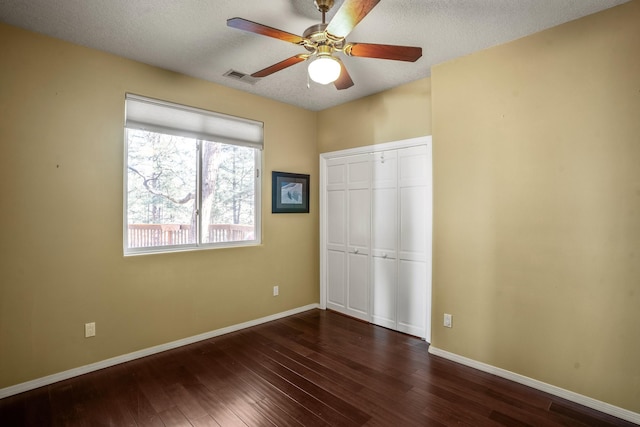 unfurnished bedroom featuring ceiling fan, a closet, dark wood-type flooring, and a textured ceiling