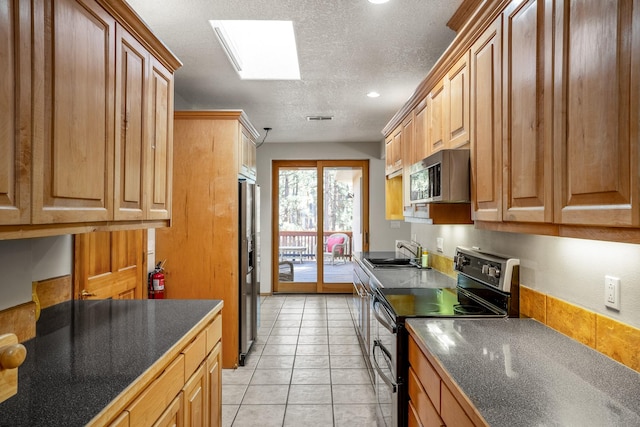 kitchen with a skylight, a textured ceiling, stainless steel appliances, sink, and light tile patterned flooring