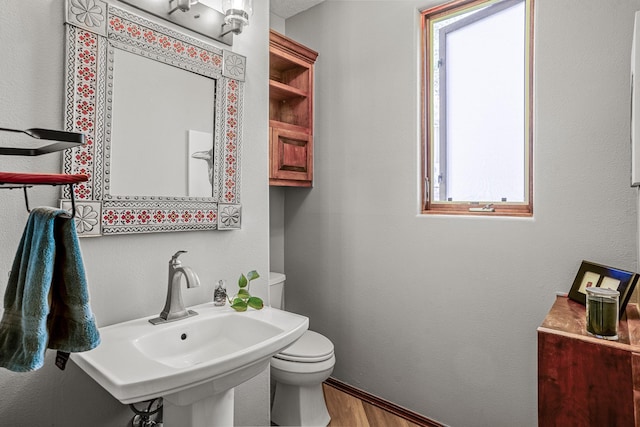 bathroom with toilet, sink, a healthy amount of sunlight, and wood-type flooring