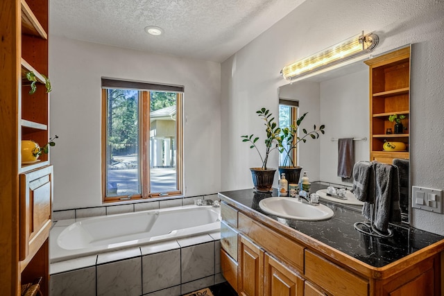 bathroom with a wealth of natural light, vanity, a relaxing tiled tub, and a textured ceiling