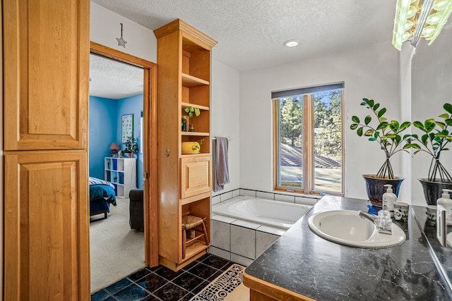 bathroom featuring tiled tub, vanity, and a textured ceiling