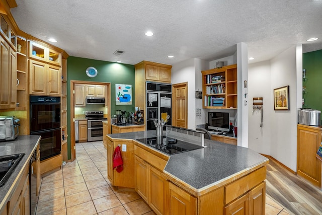 kitchen with sink, a textured ceiling, a center island with sink, light tile patterned flooring, and black appliances