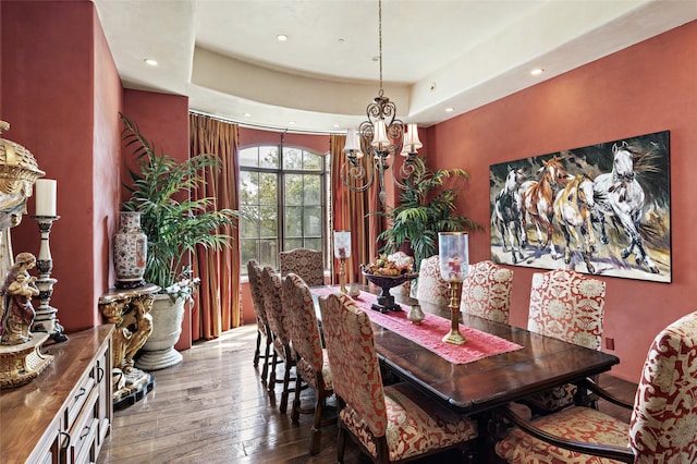 dining area with hardwood / wood-style flooring, a raised ceiling, and a notable chandelier