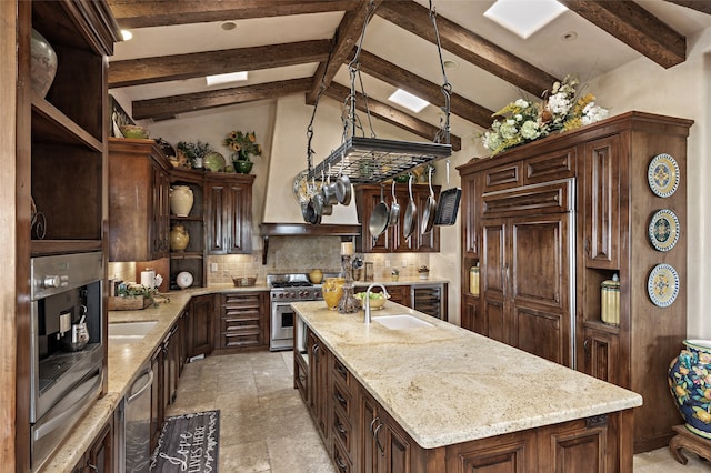 kitchen with high end appliances, a kitchen island with sink, vaulted ceiling with beams, decorative light fixtures, and dark brown cabinetry