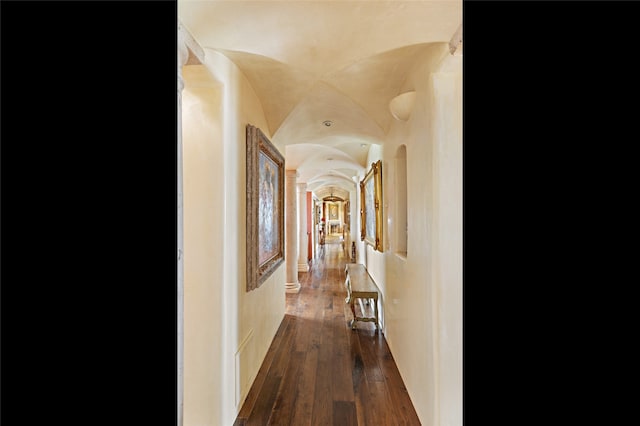 hallway with lofted ceiling, ornate columns, and dark wood-type flooring