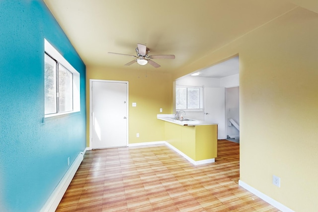 kitchen with ceiling fan, kitchen peninsula, sink, and light hardwood / wood-style flooring