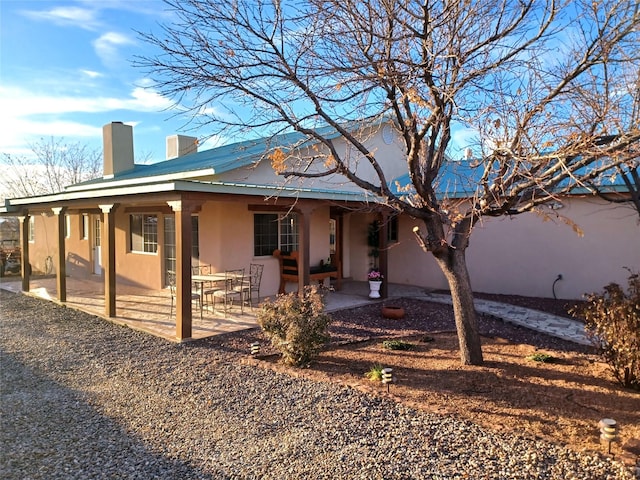 view of front of house with metal roof, a chimney, a patio area, and stucco siding