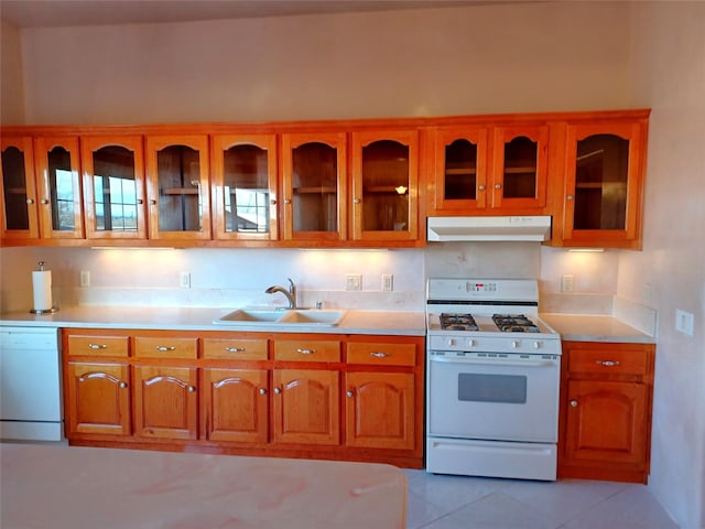 kitchen with brown cabinets, light countertops, a sink, white appliances, and under cabinet range hood