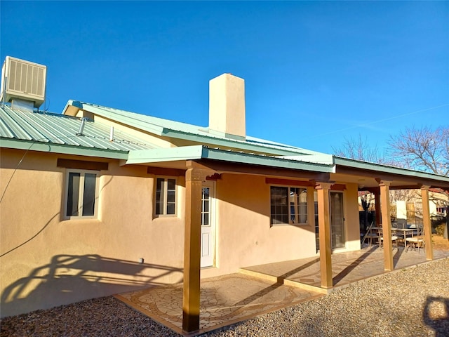 back of house with a patio area, a chimney, metal roof, and stucco siding