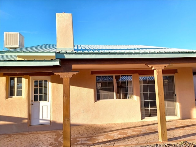 view of property exterior featuring metal roof, a chimney, cooling unit, and stucco siding