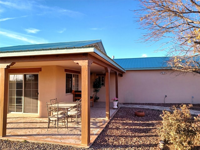 rear view of house featuring outdoor dining space, metal roof, a patio, and stucco siding