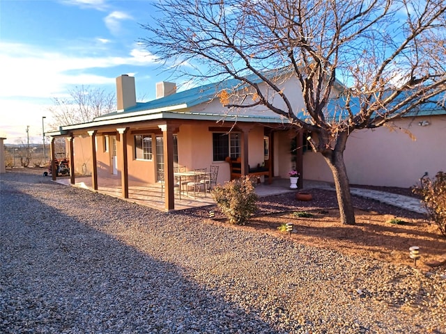 exterior space with a patio area, metal roof, a chimney, and stucco siding