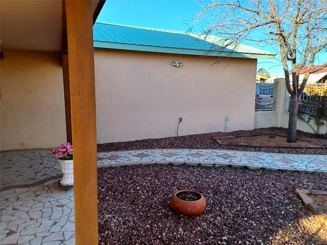 view of side of home with metal roof, a patio area, fence, and stucco siding