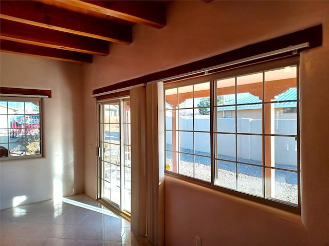 doorway with dark tile patterned floors, beam ceiling, and a healthy amount of sunlight