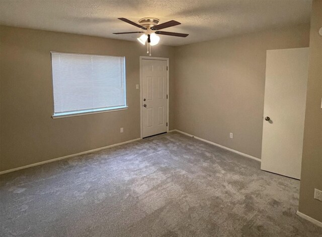 empty room with ceiling fan, light colored carpet, and a textured ceiling