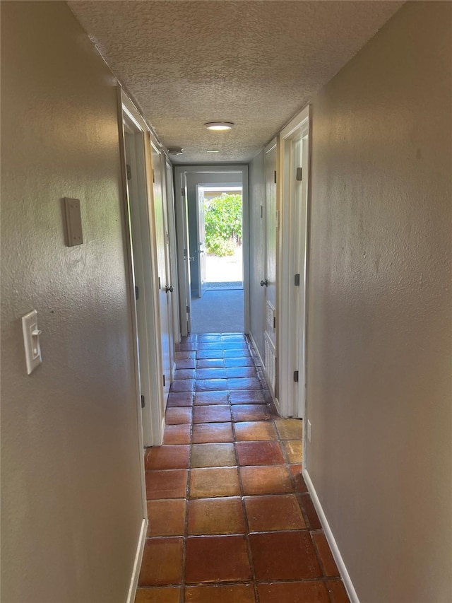 corridor with a textured ceiling and dark tile patterned flooring