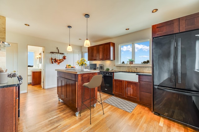 kitchen featuring light wood-type flooring, sink, black appliances, pendant lighting, and a kitchen island