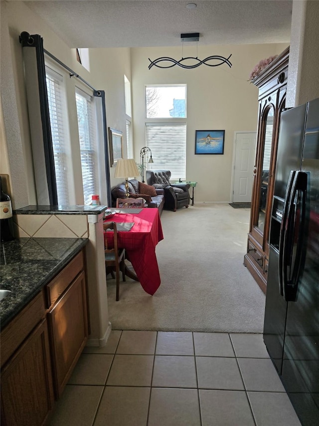 kitchen with a textured ceiling, dark stone countertops, light colored carpet, and fridge with ice dispenser